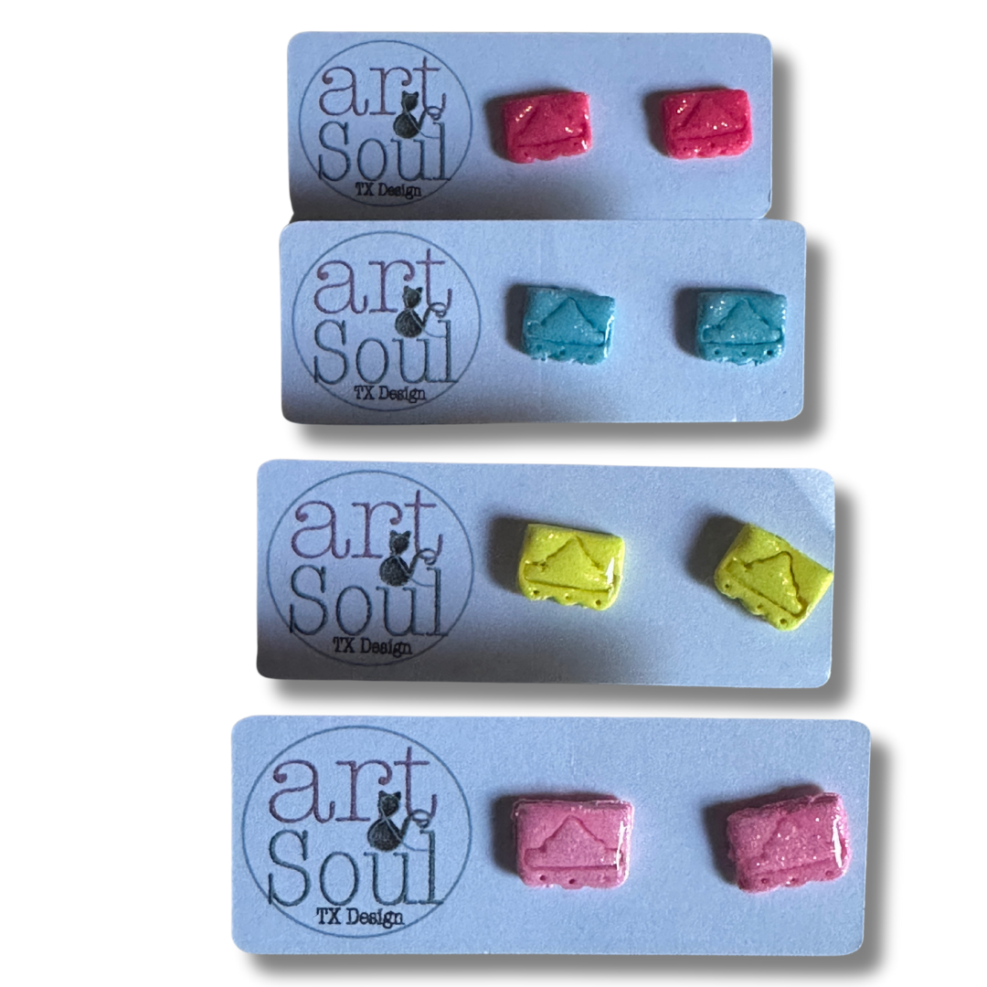 A variety pair of mini Alamo papel earrings made out of polymer clay and resin. Each pair is clipped onto Art & Souls card stock earring holder. The top pair of earrings are hot pink, below are sky blue, below are yellow, and lastly pink.