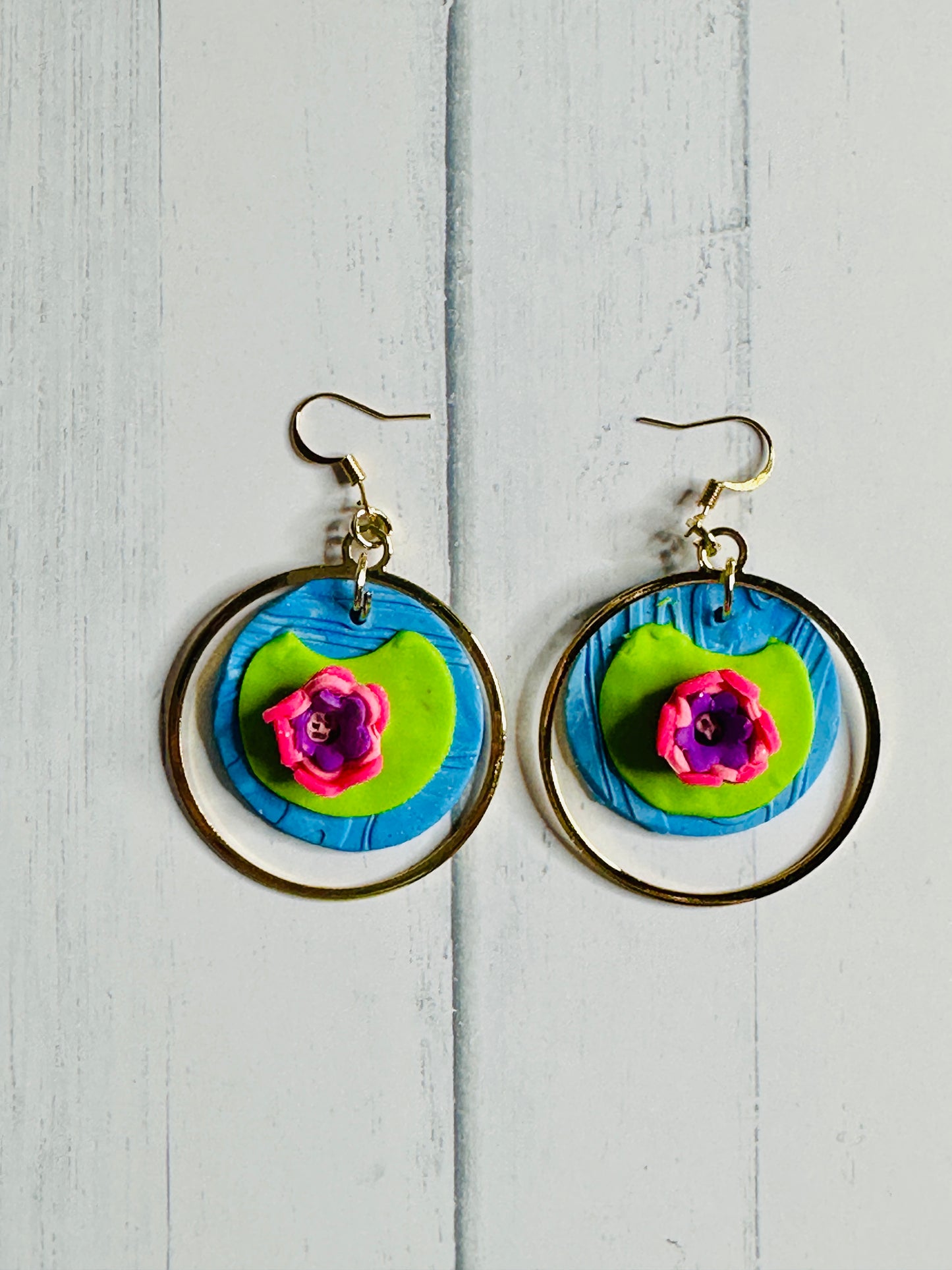 A pair of Monet Water Lilly Earrings on a white wooden table.