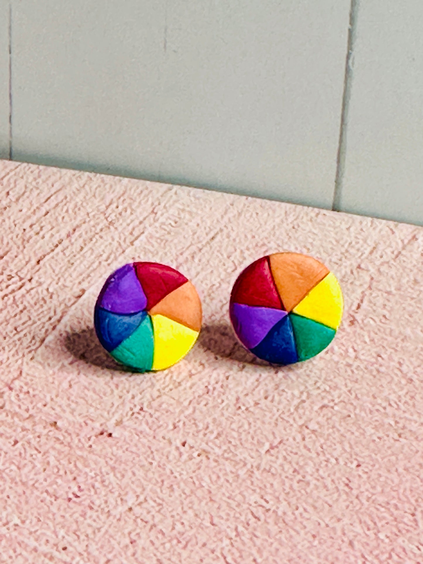Another angle of the color wheel stud earrings sitting on a pink table.