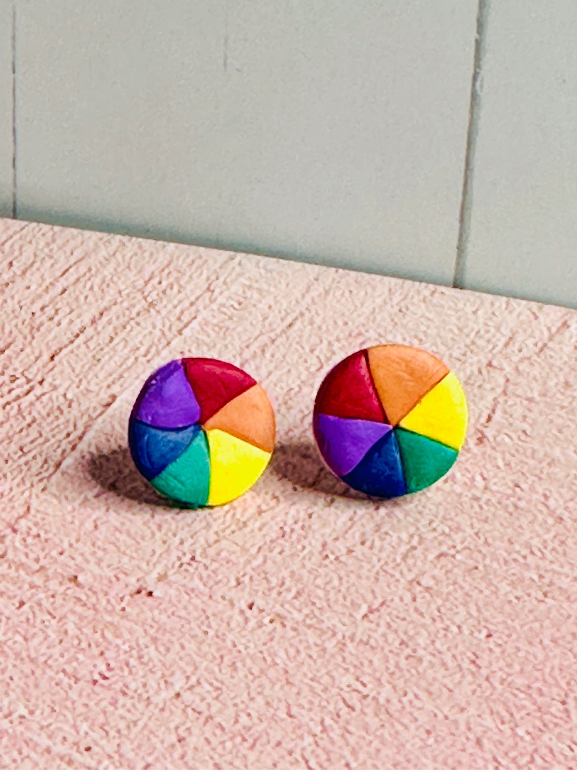 Another angle of the color wheel stud earrings sitting on a pink table.