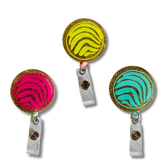 Collection of concha badge reels in various colors including pink, blue, and yellow.