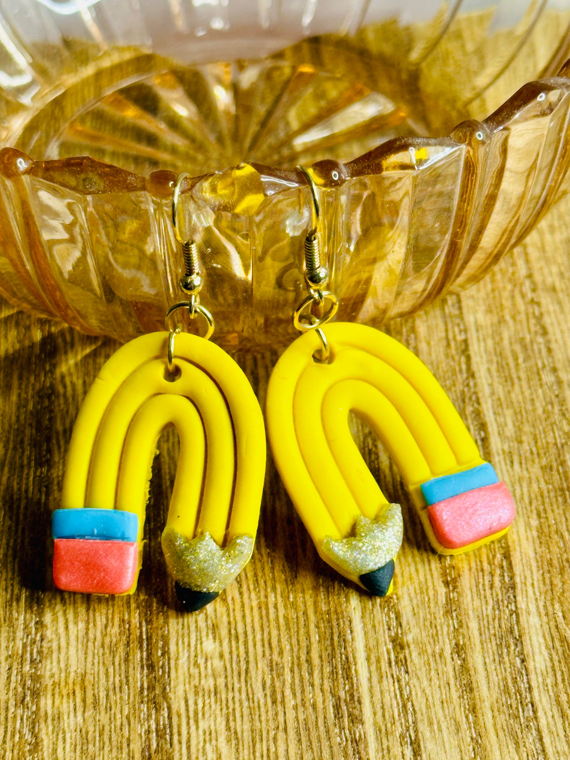 Curved Pencil Earrings draped over a pink glass bowl on a brown wooden table.