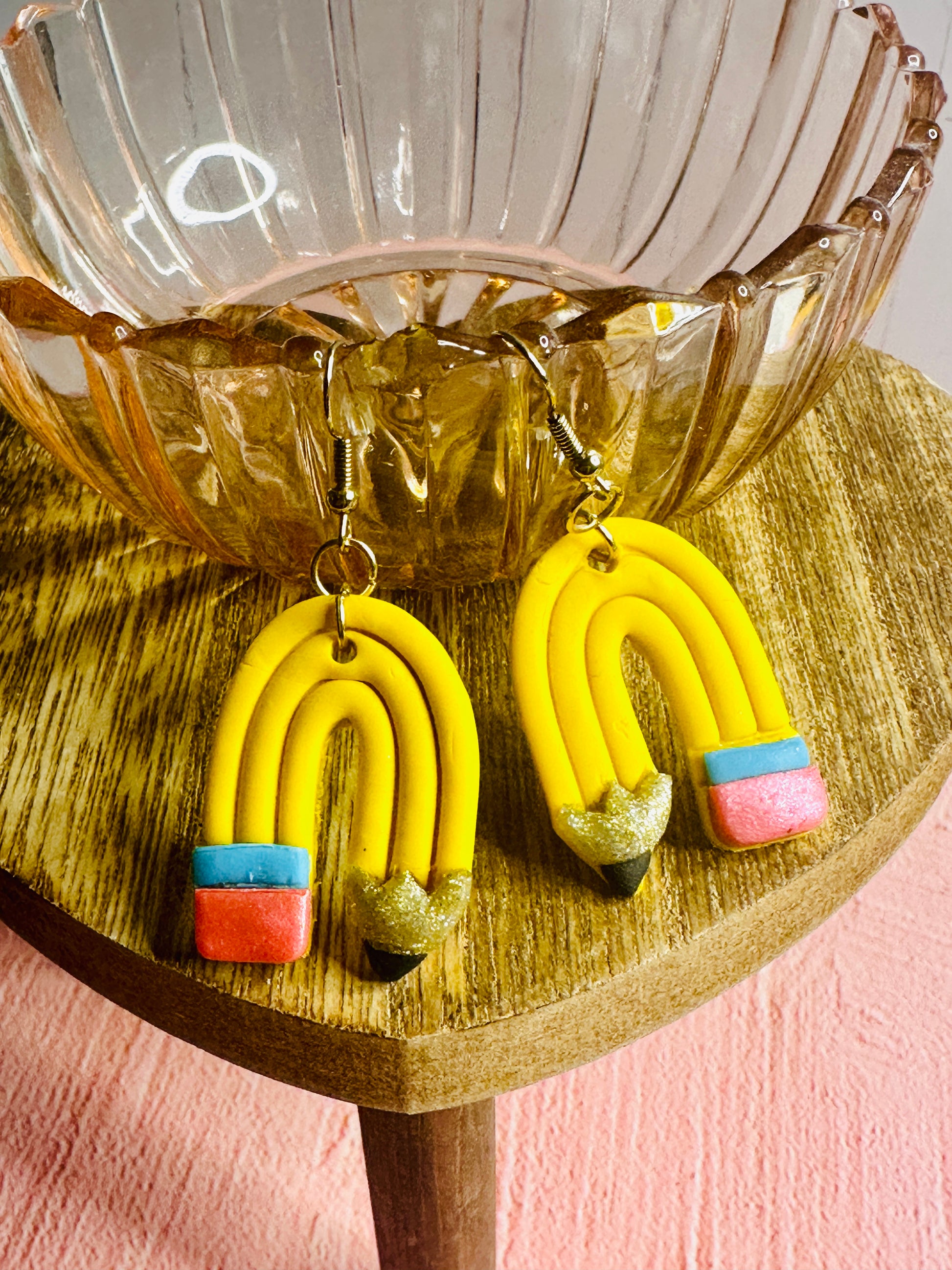 An angled view of the yellow Curved Pencil Earrings draped over a pink glass bowl on an elevated brown table.