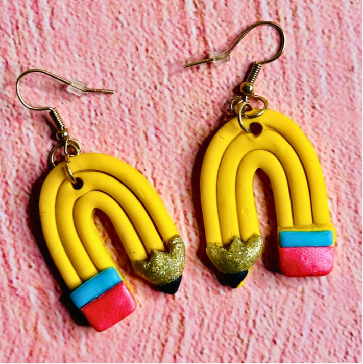 A close-up of the curved pencil earrings.  The earrings show yellow pencils bent like a rainbow, with pink erasers, golden wood, and black pencil tips.