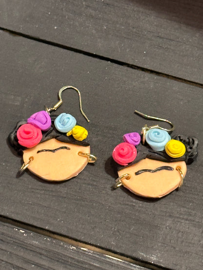 An angled view of Frida Kahlo earrings sitting on a black table.