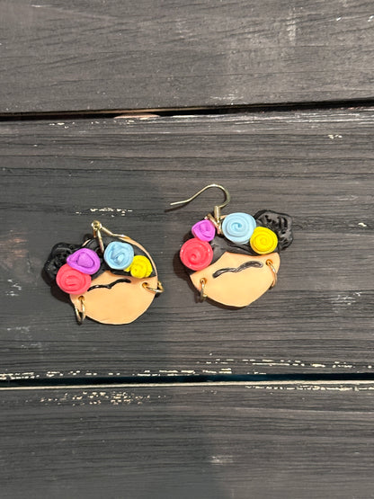 A straight view of the Frida Kahlo earrings sitting on a black wooden table.