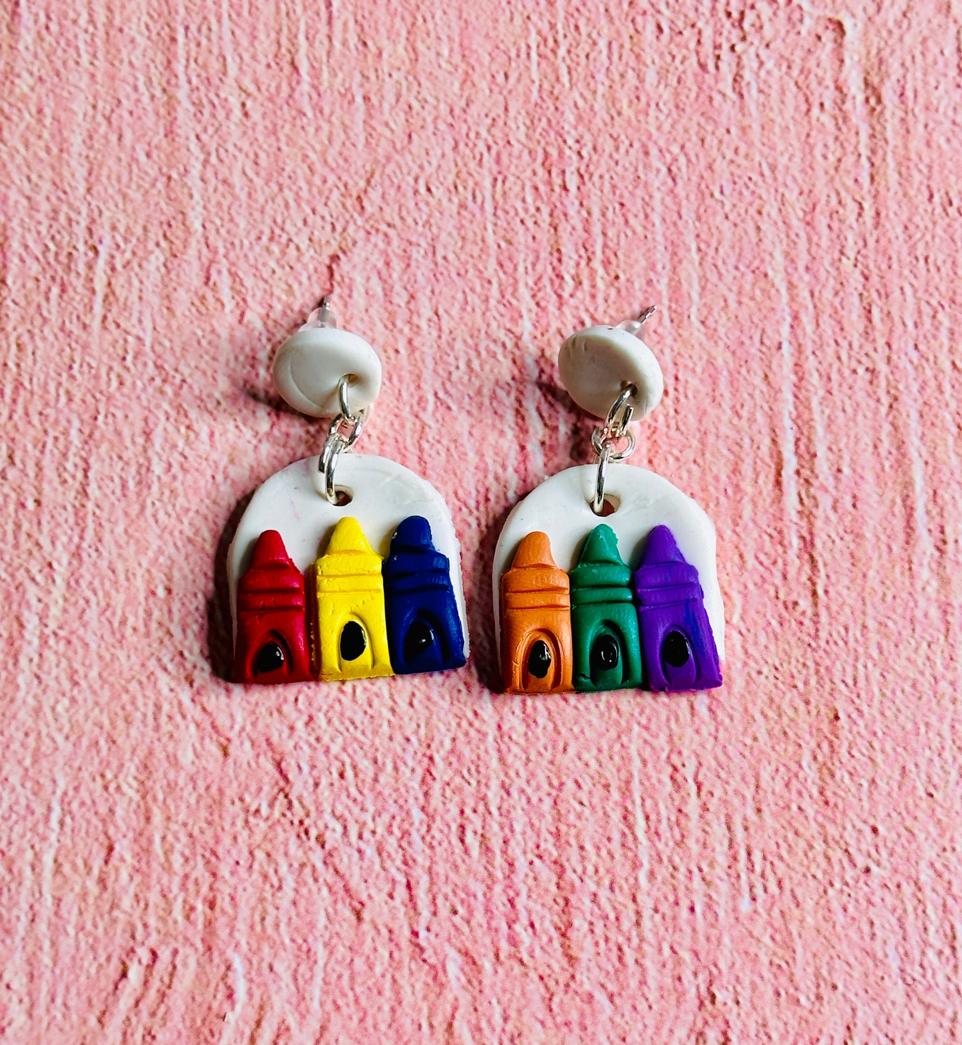 The Primary Color Earring is on the left, with red blue , and yellow crayons on a white background.  The Secondary Color Earring is on the right with orange green, and purple crayons on a white background.