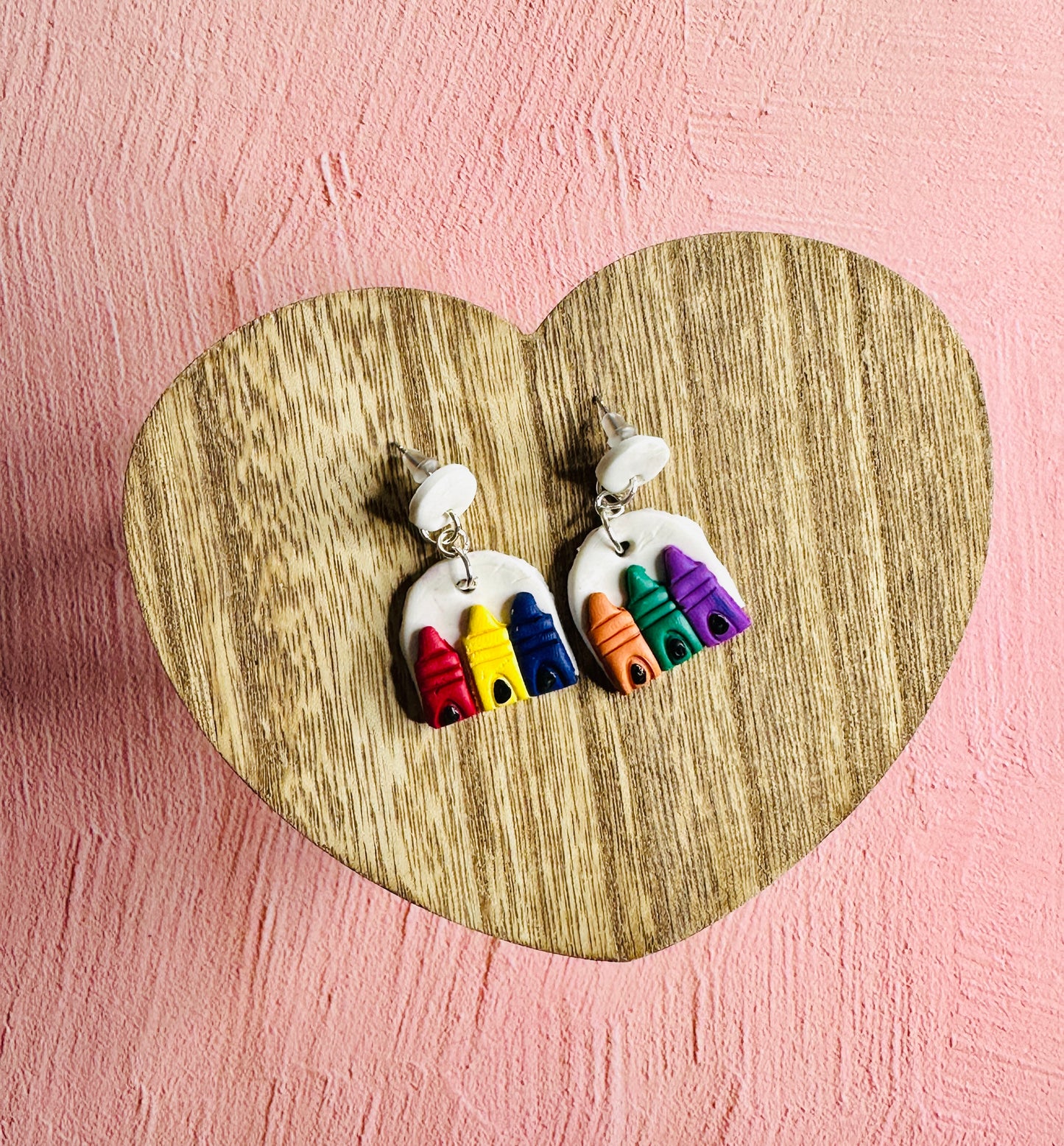 A pair of Primary and Secondary Color Earrings sitting on a brown, wooden, heart-shaped table surrounded by a pink backdrop.