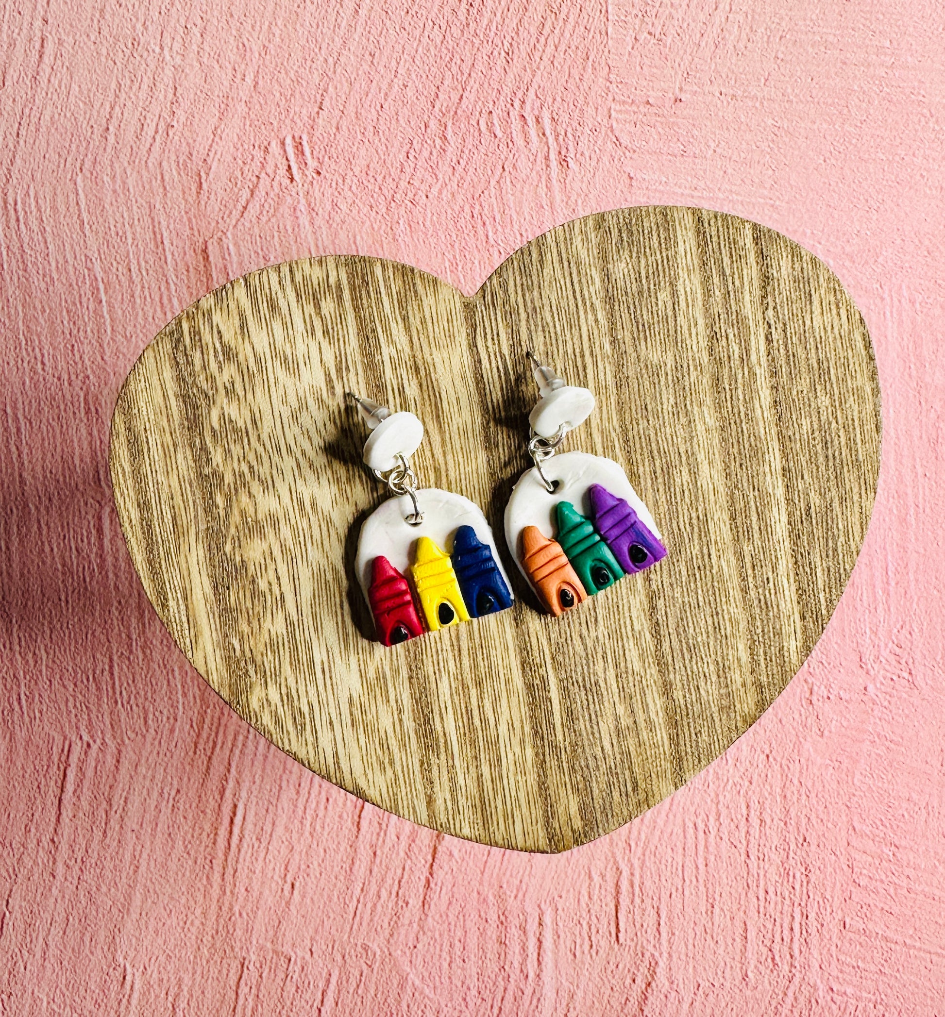 A pair of Primary and Secondary Color Earrings sitting on a brown, wooden, heart-shaped table surrounded by a pink backdrop.