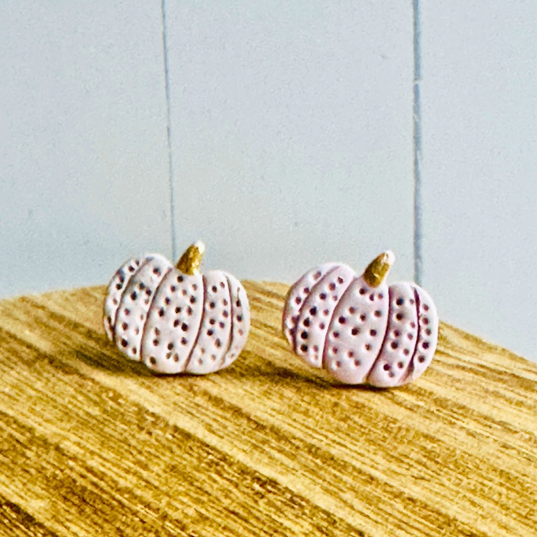 The purple pumpkin stud earrings sitting on a wooden table.