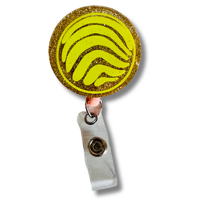 A close up of the yellow concha badge reel.  A yellow vinyl concha sits on top of a golden glitter resin background.  There is also a close-up of the secure clip mechanism on the back of the concha-shaped badge reel.